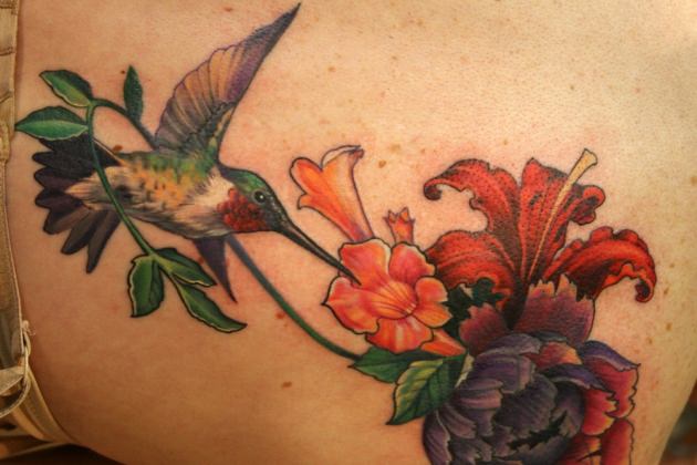A beautiful tattoo of a hummingbird sipping nectar from a bouquet of