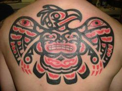 A tribal tattoo of an Aztec eagle with a grinning face and eye designs