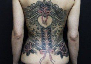 This corset tattoo has a heart at its center, surrounded by feminine tattoo designs like lace and ribbons