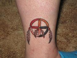 An ankle tattoo of a native American medicine wheel with a cross at it center and surrounded by feathers