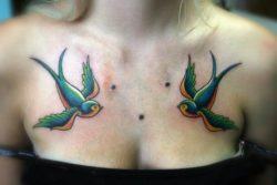 A tattoo of two swallows on a girls chest. The traditional tattoo designs are displayed with body bolts