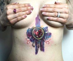 A Peter Aurisch abstract tattoo between a womans breasts that features a heart jewel with ribbons