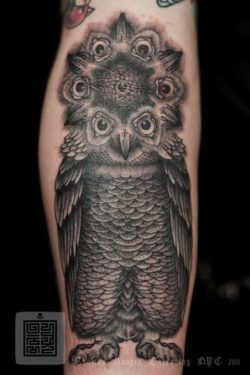 A black ink tattoo by Thomas Hooper that uses the face of an owl to create a mandala flower