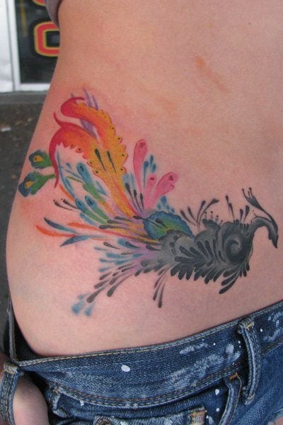 A colorful, creative abstract tattoo of a peacock bird decorates this girl's hip