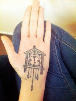 A palm tattoo of a cuckoo clock that stretches from the palm of the hand to the wrist.