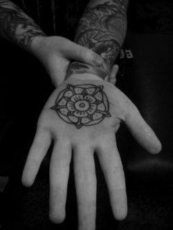 A tattoo on the palm of the hand showing a mandala flower design