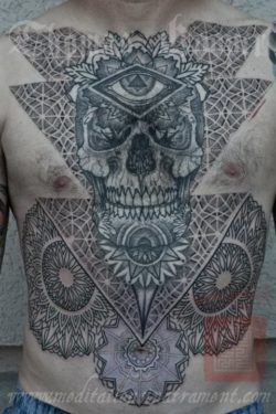 Sacred geometry and mandalas decorate this tattoo of a skull, eye of god and flowers