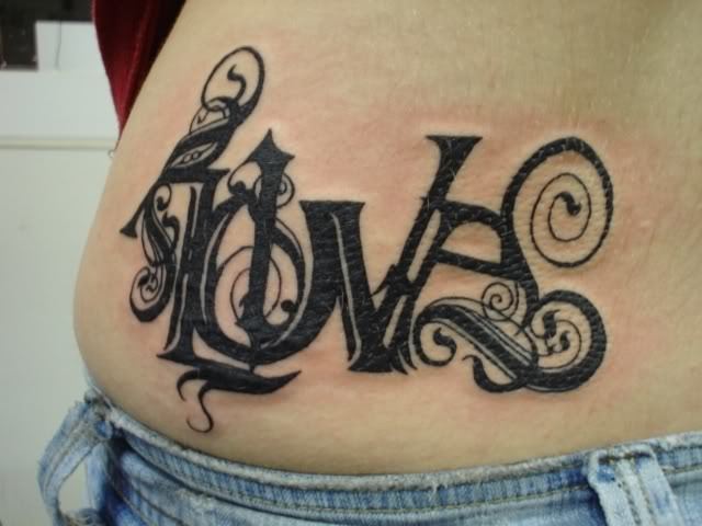 A tattoo of the word love in Gothic font with floral decorations