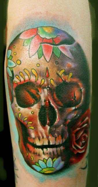 A Day of the Dead tattoo that shows a realistic human skull painted with flowers and patterns
