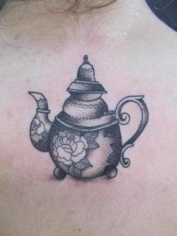 A detailed tattoo of a tea pot decorated with roses on the back of the neck