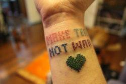 This creative tattoo design uses cross stitch to spell out the phrase Make Tea Not War