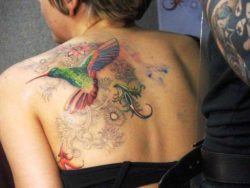 This floral tattoo shows a colorful hummingbird on a background of lacy flowers and curls