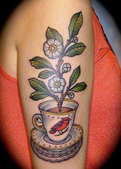 This tattoo design shows a peach blossom branch growing out of a cup of tea with a red cardinal bird on the cup