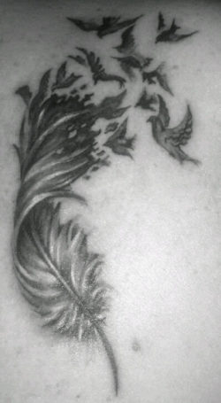 A beautiful black and white tattoo of a feather dissolving into a flock of birds
