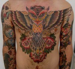 A large chest tattoo of a flying owl holding a diamond, surrounded by rose flowers