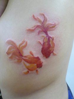An abstract tattoo design of two goldfish. The tattoo artist has left some areas un-inked to create the impression of shiny scales