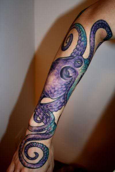 A blue and purple octopus tattoo that flows down the arm, ending with a curled tenatcle on the back of the hand