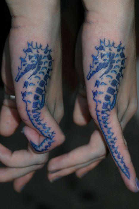 A blue ink tattoo of a seahorse on the side of the hand. When the tattoo owner curls her finger, the tail of the seahorse curls too