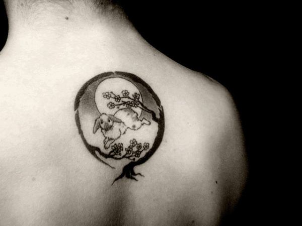 A tattoo of a hare or rabbit jumping in front of the moon under a cherry blossom tree
