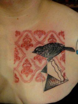 A small bird inspects a paisley pattern in this artistic tattoo by Xoil