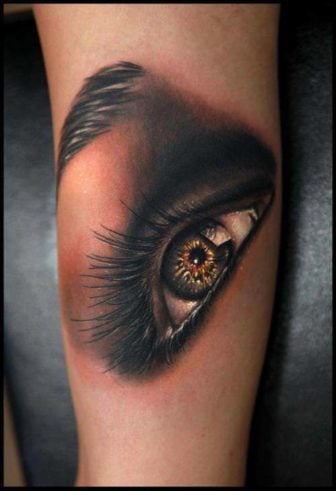 A stunning photo realistic tattoo of an eye by Rich Pineda with gold tones and smoky shadows