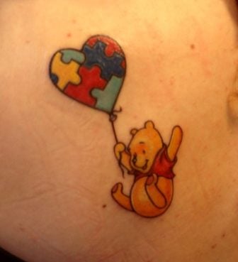 A super cute tattoo of Winnie the Pooh flying with the help of a puzzle patterned balloon