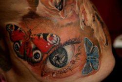 This feminine tattoo of a realistic eye surrounded by butterflies is a combination of symbols