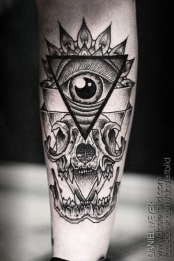 A human eye encased in a triangle and sacred geometry sits above a grinning animal skull in this tattoo by Daniel Meyer