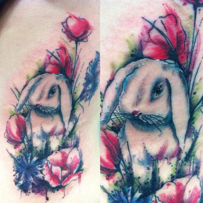 A peaceful bunny rabbit sits among poppy flowers in this artistic watercolor tattoo by Mel Wink