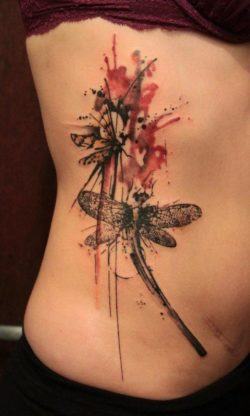 Abstract dragonflies flutter together in this splashy watercolor tattoo by Gene Coffey