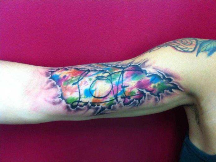 Torn flesh reveals the word love surrounded by watercolor splatters in this artistic tattoo by Mel Wink