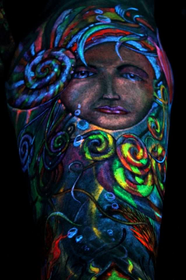 A female face peeks from between nautilus shells in this fantasy UV tattoo on Glowrious George