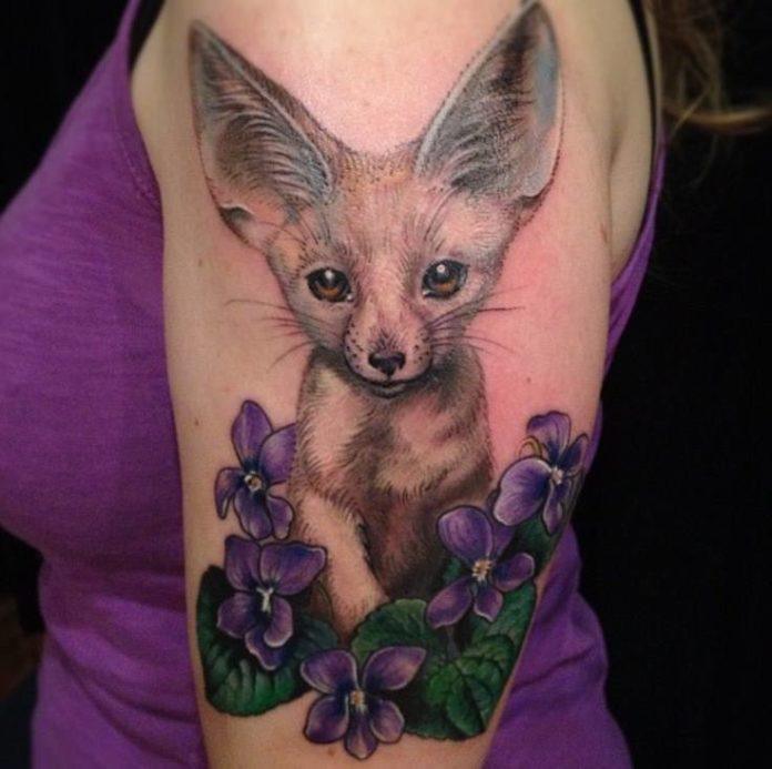 A cute bat eared fox peeks out from among flowers in this feminine tattoo design by Esther Garcia