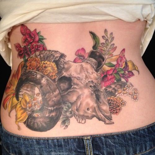 Life and death merge in this tattoo of an animal skull surrounded by flowers by Butterfat studios
