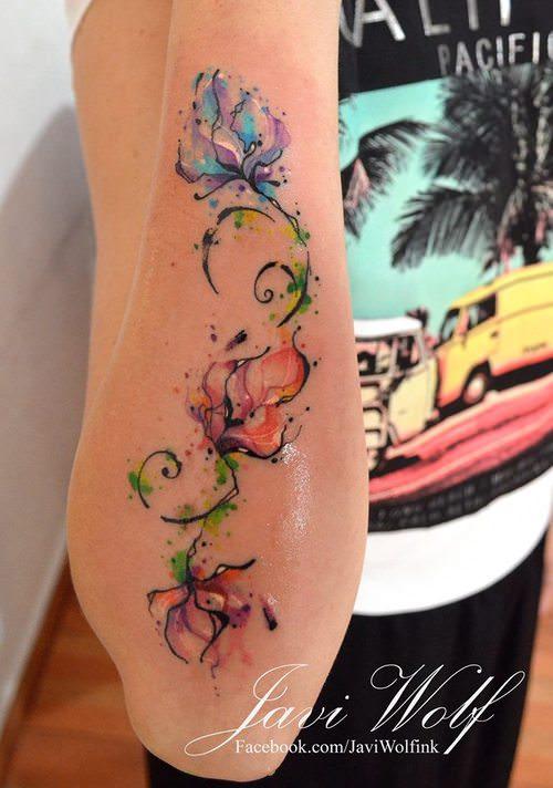 Flowers decorate this girls arm from wrist to elbow in a watercolor tattoo by Javi Wolf