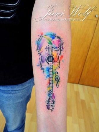 Javi Wolf gives his client a beautiful and symbolic watercolor tattoo of a guitar with a treble clef
