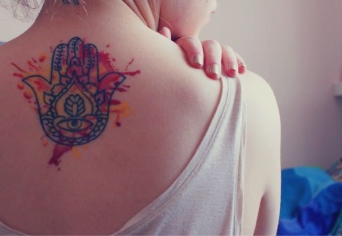 This spiritual Hamsa hand tattoos has creative watercolor splatters to add visual appeal