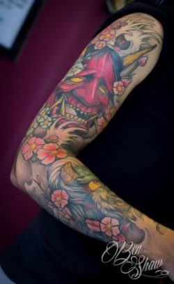 A Japanese demon grins out from behind the cover of cherry blossoms and waves in this life and death tattoo by Ben Shaw