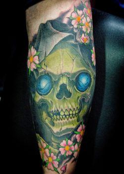 A hooded skull with glowing eyes watches the world from behind a cluster of cherry blossoms in this gothic tattoo by Ben Shaw.