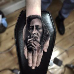 This photo realistic hand tattoo shows Bob Marley smoking a joint.