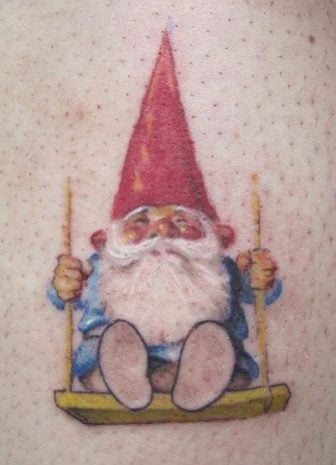 This adorable tattoo shows a rosy cheeked gnome on a swing