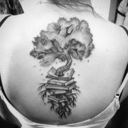 A tree grows out of a pile of books in this black ink tattoo