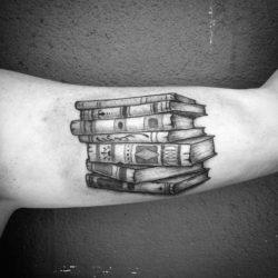 This beautiful black ink tattoo shows a professionally inked pile of books