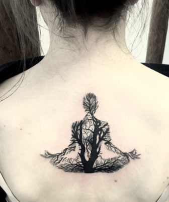 This fantastic back tattoo by tattoo artist Kradmelder Dieter uses vein-like tree branches to reveal the form of a woman sitting and meditating